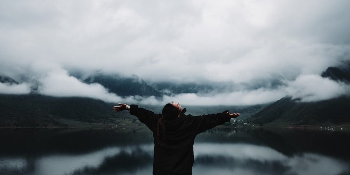A person enjoys a sense of freedom by a misty mountain lake, embracing nature's tranquility.