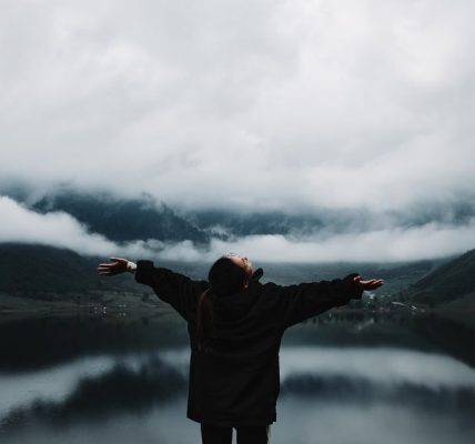 A person enjoys a sense of freedom by a misty mountain lake, embracing nature's tranquility.