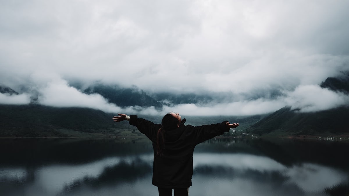 A person enjoys a sense of freedom by a misty mountain lake, embracing nature's tranquility.